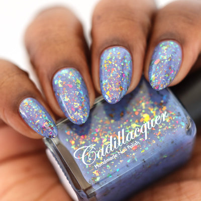 Cadillacquer Don't Worry purple pink chameleon iridescent crelly nail polish, bottle held with four-nail swatch, medium-deep skin, studio lighting