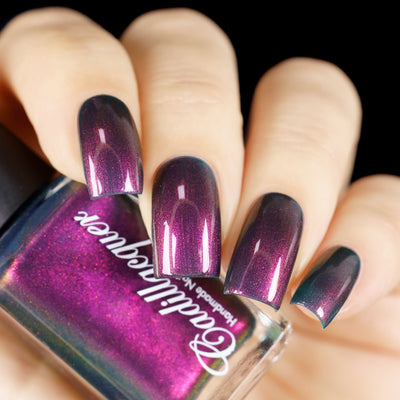 Multichrome shimmer Cadillacquer nail polish in Fear What You Will Become, shown swatched on four square nails alongside the bottle, shifting from deep dark plum-teal at rest through magenta and burnt-orange shimmer at angle, with the bottle face displaying vivid magenta and the bottle edge revealing the murky teal base, light skin tone, studio lighting, swatched by @yyulia_m