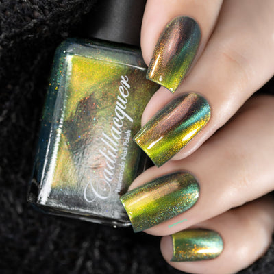 Magnetic multichrome holographic Cadillacquer nail polish in I Found A Place, shown as a hand swatch on five square nails with a bottle alongside, nails shift from deep teal field through olive-lime and chartreuse-gold magnetic band to burnt copper-red aurora flash, with fine holographic shimmer throughout, light-medium skin tone, studio lighting, swatched by @serpentine13