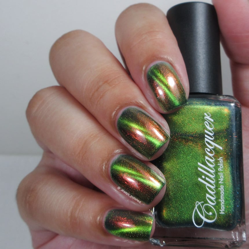 Magnetic multichrome Cadillacquer nail polish in I Found A Place, shown on eight short squoval nails with a dark olive-green field and a bright lime-yellow magnetic stripe, shifting through copper-red and orange aurora shimmer at angles, held alongside the polish bottle, on light skin tone, under studio lighting, swatched by @_always_polished_
