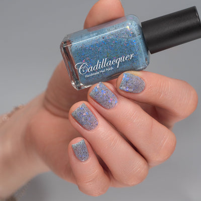 Cadillacquer Just Breathe pastel blue iridescent crelly nail polish, bottle held with four-nail swatch, light skin, studio lighting