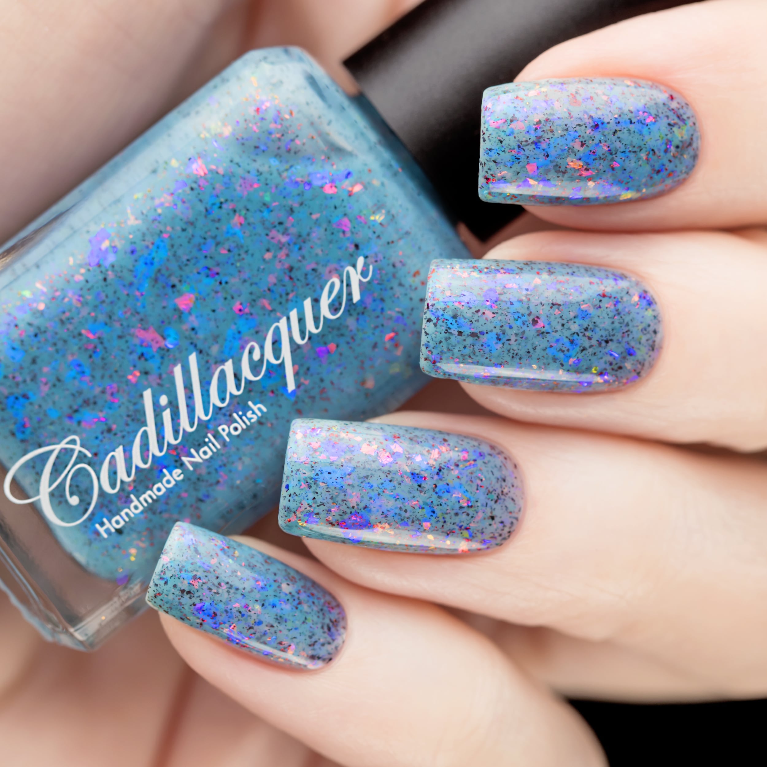 Cadillacquer Just Breathe pastel blue iridescent crelly nail polish, bottle held with four-nail swatch, light skin, studio lighting
