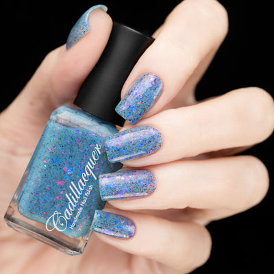 Cadillacquer Just Breathe pastel blue iridescent crelly nail polish, bottle held with four-nail swatch, light skin, studio lighting