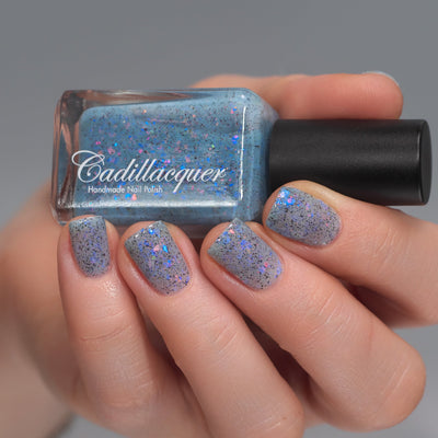 Cadillacquer Just Breathe pastel blue iridescent crelly nail polish, bottle held with four-nail swatch, light skin, studio lighting