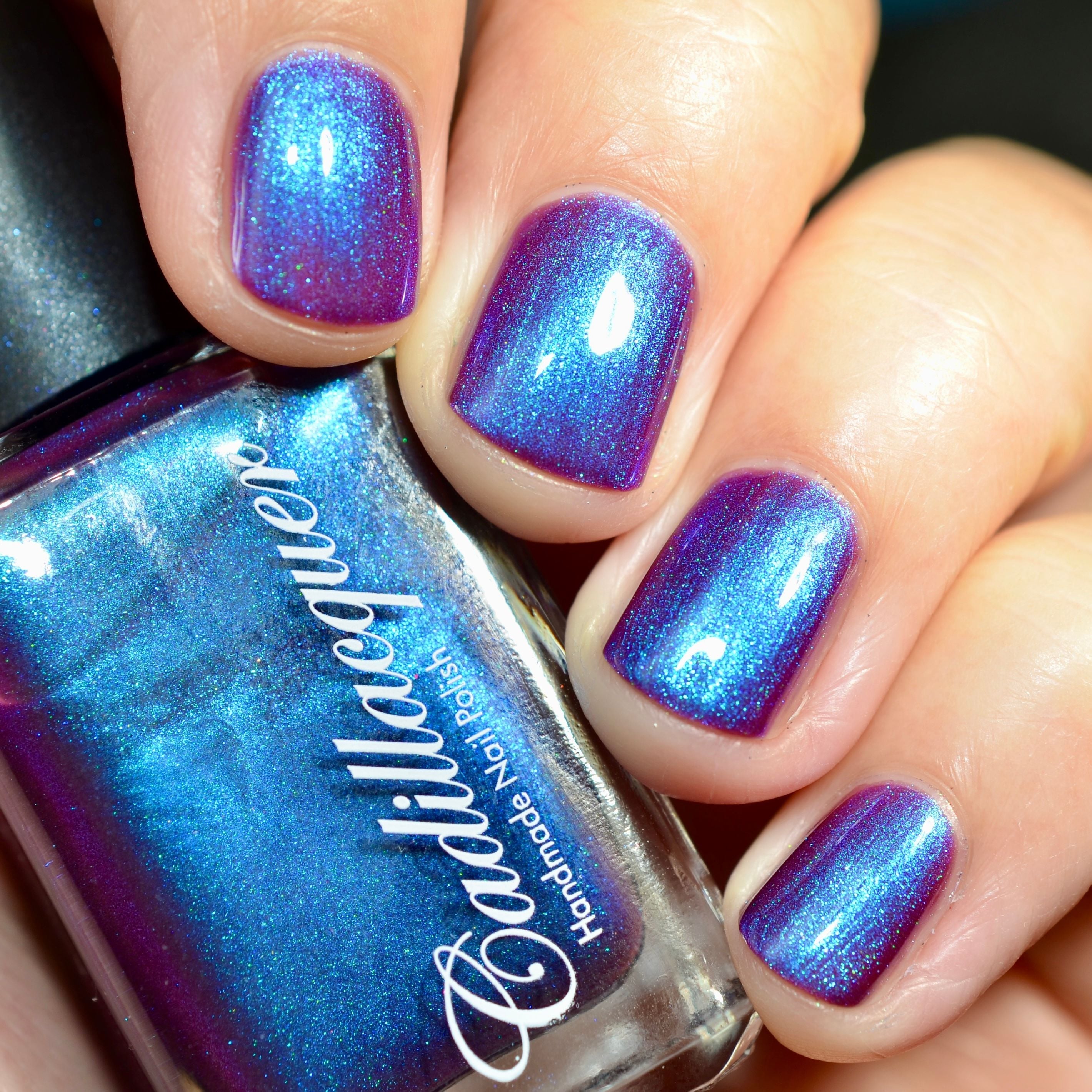 Multichrome shimmer Cadillacquer nail polish in Keep Doubting, swatched on five short squoval nails held alongside the bottle, shifting from deep mulberry-violet at rest to vivid cerulean blue under direct flash, with teal-green micro-sparkle visible, light skin tone, direct flash lighting, swatched by @caitlinswatches