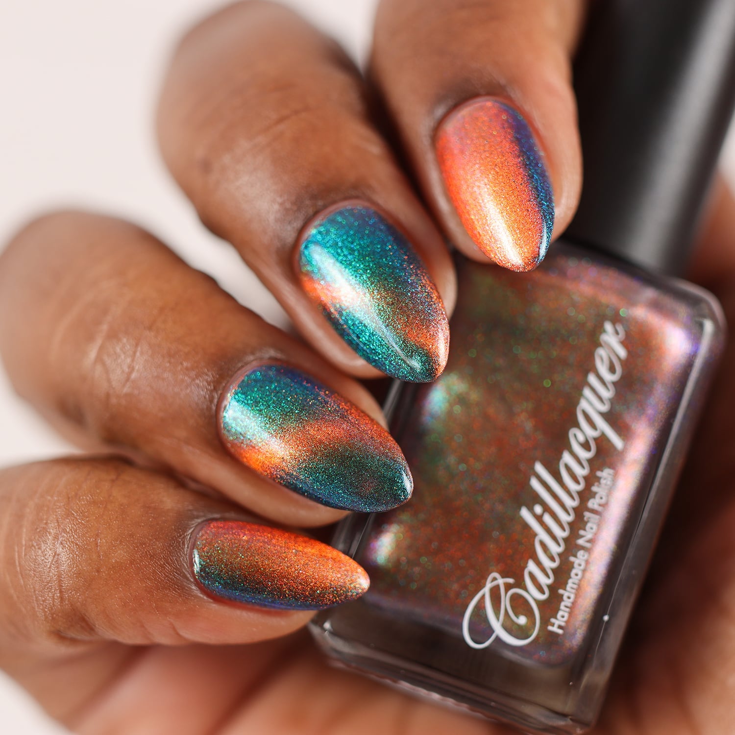 Multichrome magnetic shimmer Cadillacquer nail polish in Once You See It, swatched on five almond-shaped nails showing a dramatic colour shift from vivid copper-orange at the magnetic band to deep teal-green and blue-indigo in the field, packed with fine iridescent aurora shimmer, rich skin tone, studio lighting, swatched by @doseoflolade