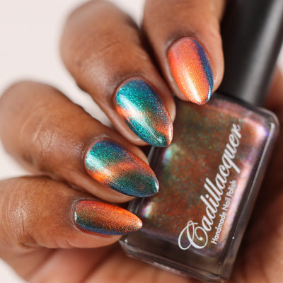 Multichrome magnetic shimmer Cadillacquer nail polish in Once You See It, swatched on five almond-shaped nails showing a dramatic colour shift from vivid copper-orange at the magnetic band to deep teal-green and blue-indigo in the field, packed with fine iridescent aurora shimmer, rich skin tone, studio lighting, swatched by @doseoflolade