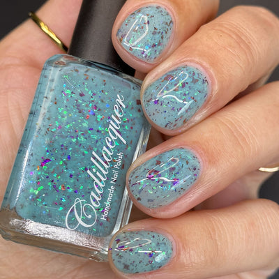 Cadillacquer Pastel Thoughts pastel teal purple chameleon iridescent crelly nail polish, bottle held with five-nail swatch, light skin, studio lighting