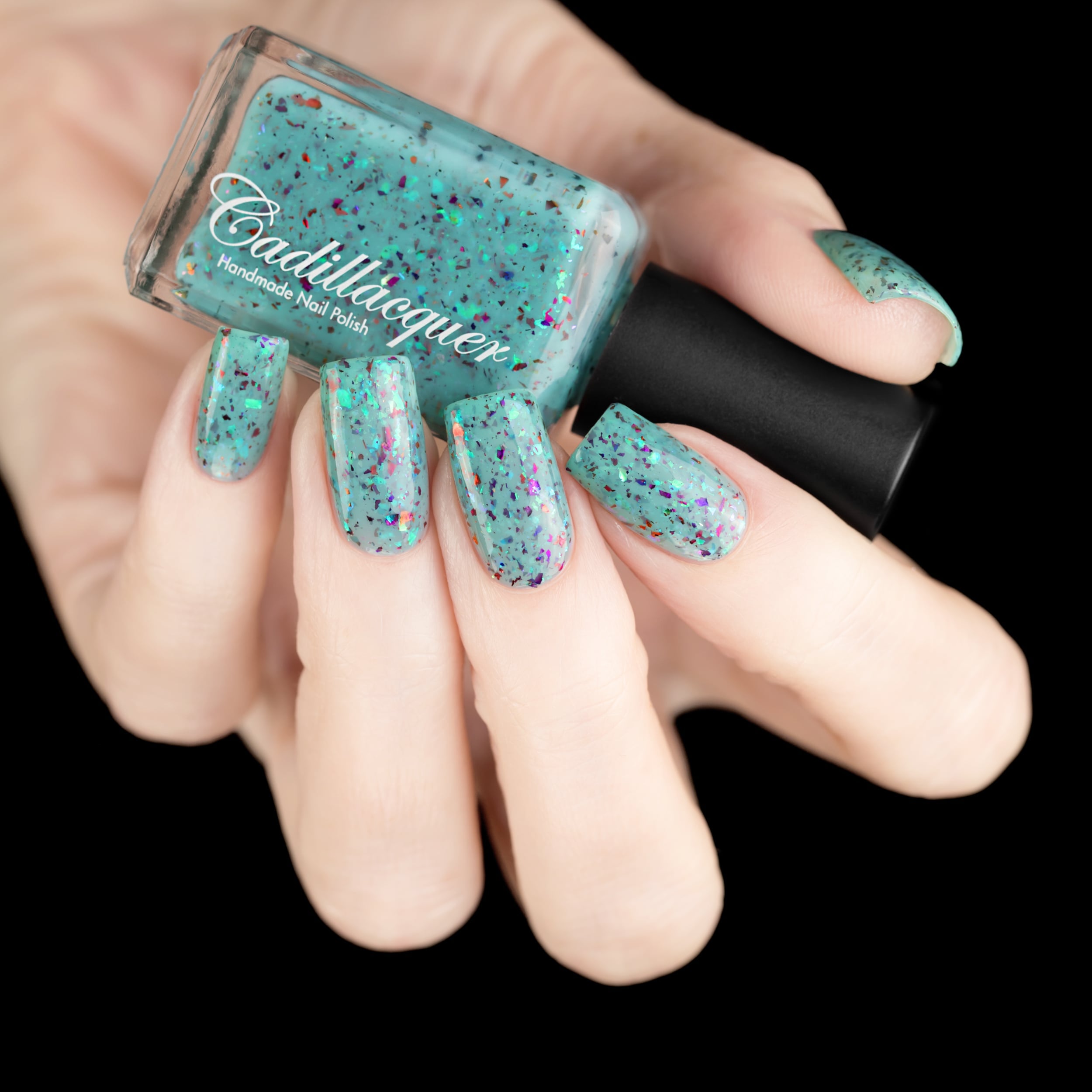 Cadillacquer Pastel Thoughts pastel teal purple chameleon iridescent crelly nail polish, bottle held with five-nail swatch, light skin, studio lighting