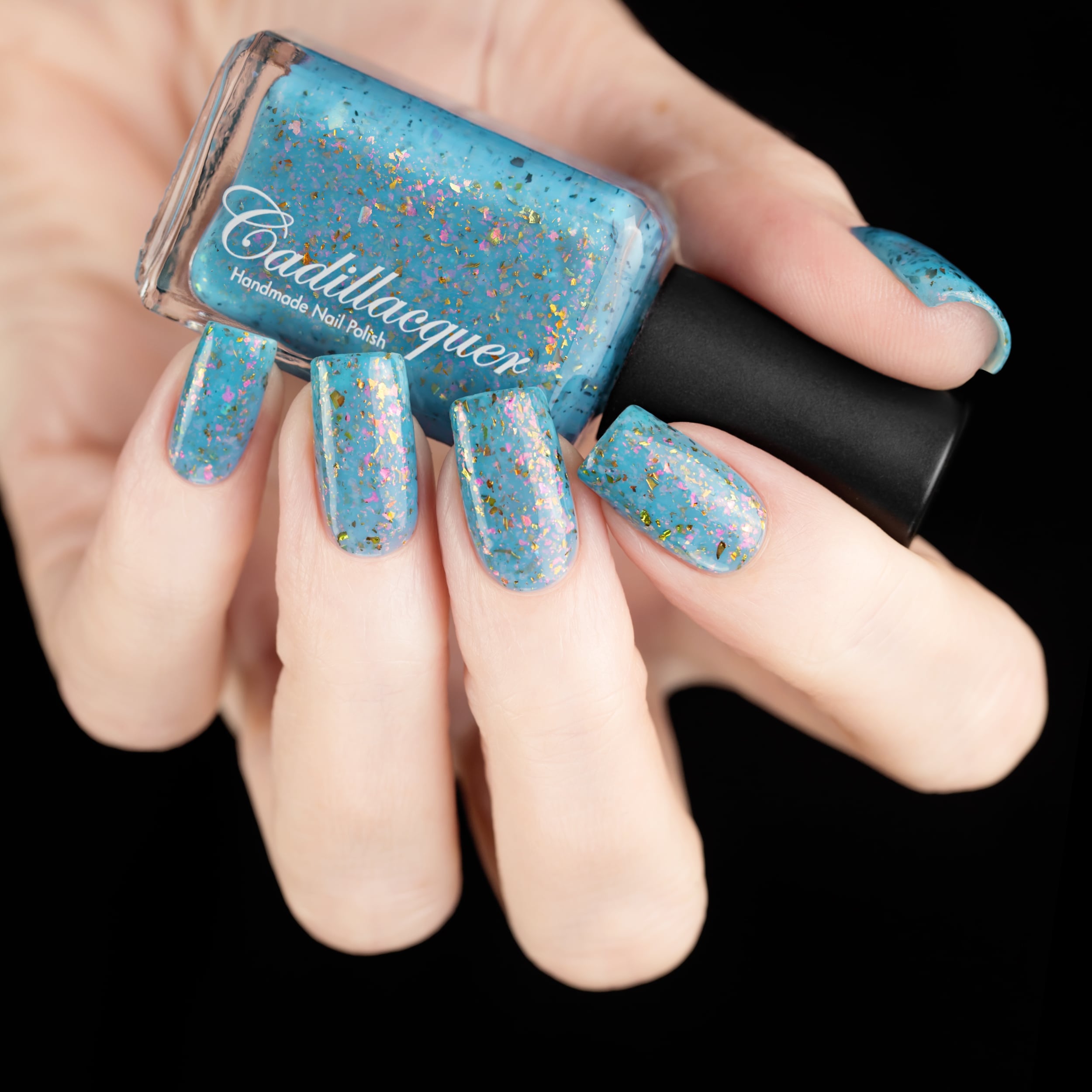 Cadillacquer Slow Mornings light blue gold chameleon iridescent crelly nail polish, bottle held with five-nail swatch, light skin, studio lighting
