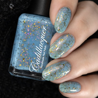 Cadillacquer Slow Mornings light blue gold chameleon iridescent crelly nail polish, bottle held with four-nail swatch, light skin, studio lighting