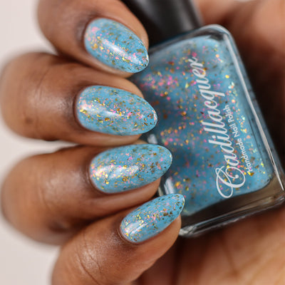 Cadillacquer Slow Mornings light blue gold chameleon iridescent crelly nail polish, bottle held with four-nail swatch, rich skin, studio lighting