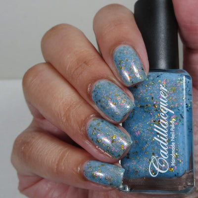Cadillacquer Slow Mornings light blue gold chameleon iridescent crelly nail polish, bottle held with four-nail swatch, light skin, bright daylight lighting