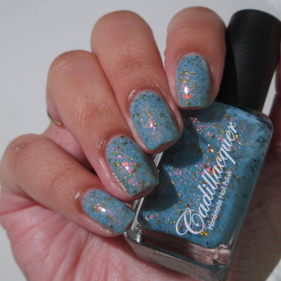 Cadillacquer Slow Mornings light blue gold chameleon iridescent crelly nail polish, bottle held with four-nail swatch, light skin, direct flash lighting