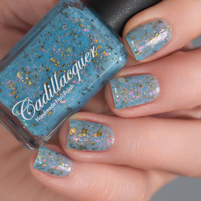 Cadillacquer Slow Mornings light blue gold chameleon iridescent crelly nail polish, bottle held with four-nail swatch, light skin, studio lighting