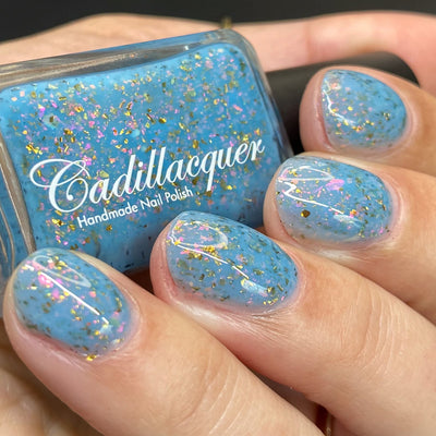 Cadillacquer Slow Mornings light blue gold chameleon iridescent crelly nail polish, bottle held with four-nail swatch, light skin, studio lighting