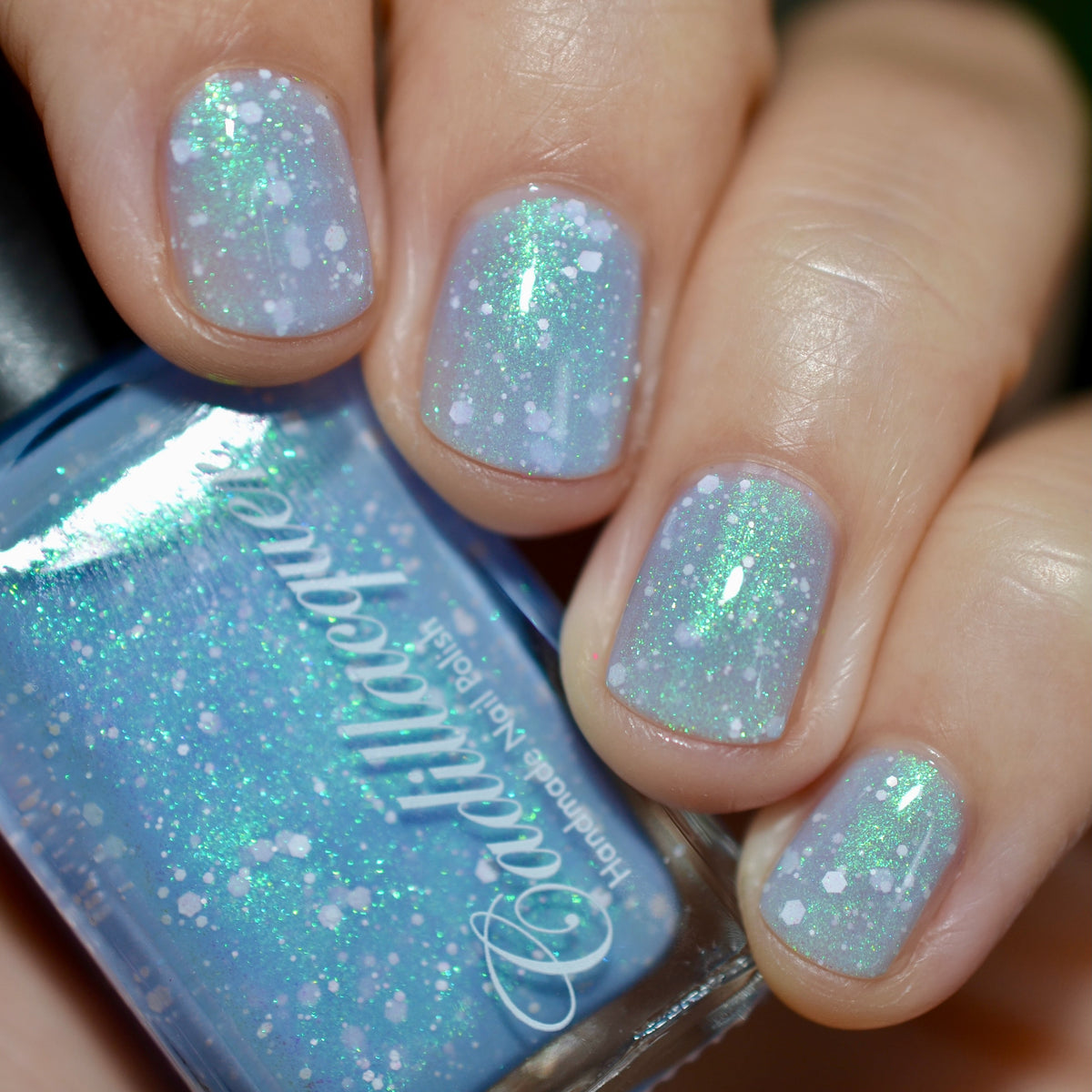 Cadillacquer Spotted Glass Frog nail polish swatched with bottle, white glitter in blue jelly
