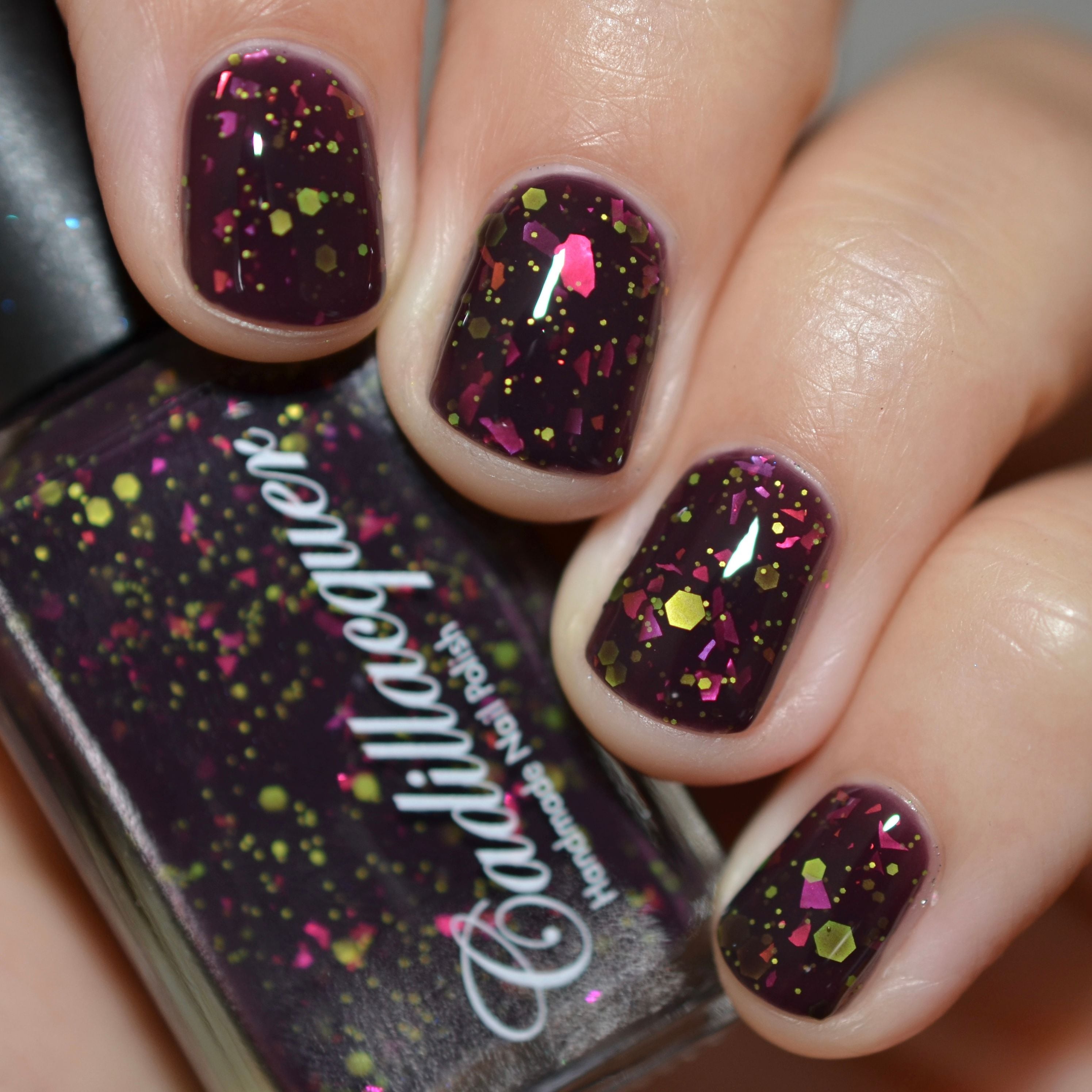 Thermal glitter-and-flake Cadillacquer nail polish in Strange Happenings, shown swatched on five short square nails and in bottle, cold-state blackened eggplant-purple base loaded with neon chartreuse matte glitter in mixed sizes and hot magenta iridescent flakes, light-medium skin tone, studio lighting, swatched by @caitlinswatches