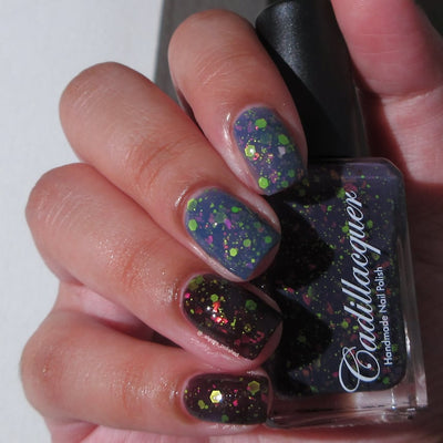 Thermal glitter and flake Cadillacquer nail polish in Strange Happenings, shown on four short natural nails with both warm (dusty blue) and cold (blackened eggplant) thermal states visible simultaneously, loaded with matte neon green hex glitter and pink iridescent flakes, with matching bottle held in hand, light-medium skin tone, indoor warm lighting, swatched by @_always_polished_
