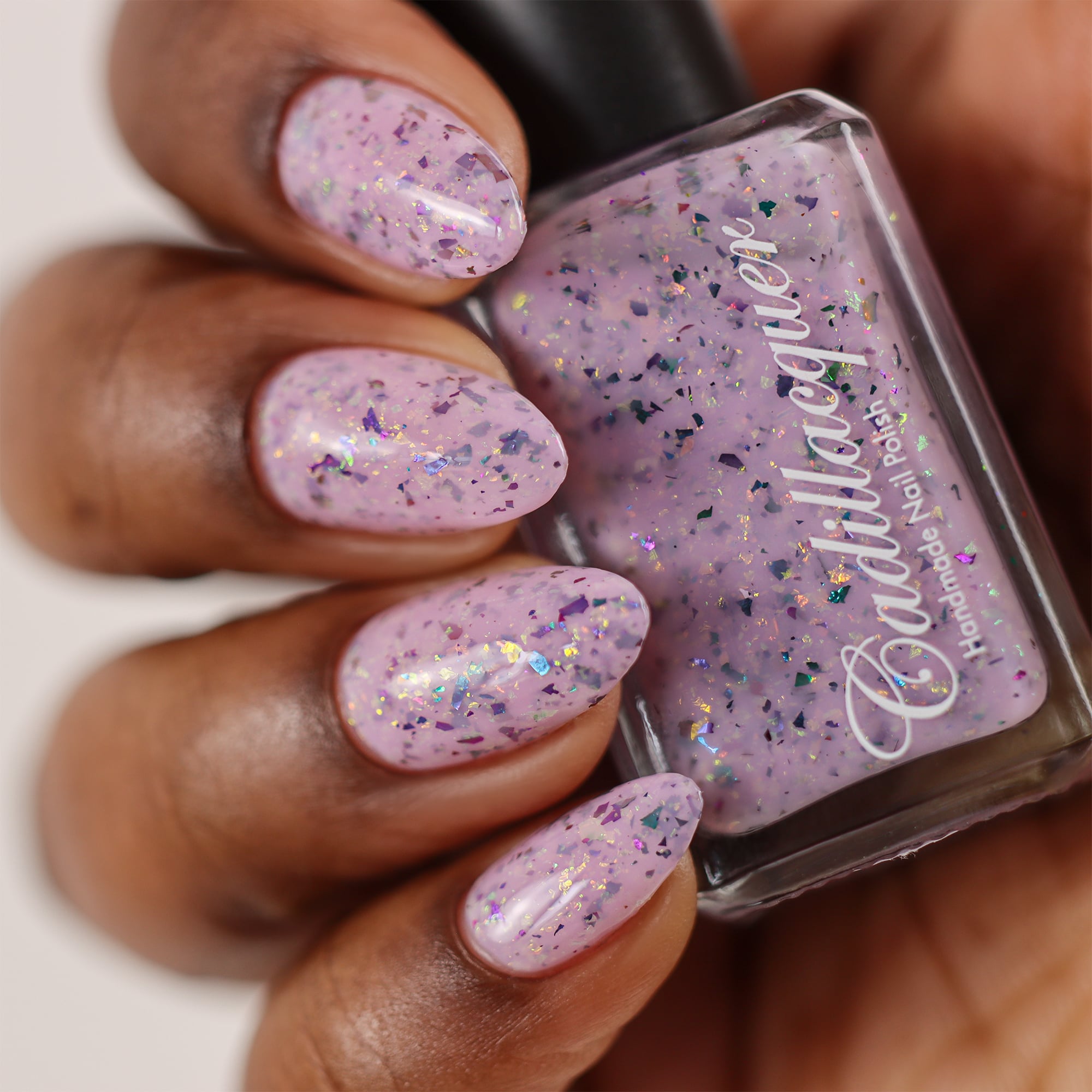 Cadillacquer Sweet Nothing pink teal chameleon iridescent crelly nail polish, bottle held with four-nail swatch, rich skin, studio lighting