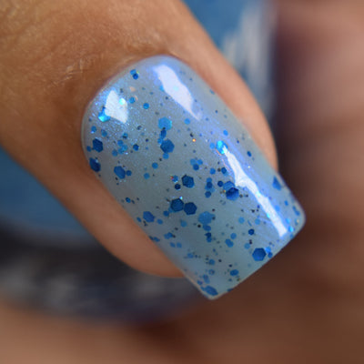 Blueberry Sanctuary by Dam Nail Polish, sheer light blue crelly with assorted metallic blue hex glitters and blue-to-purple shifting shimmer, on a medium skin tone hand