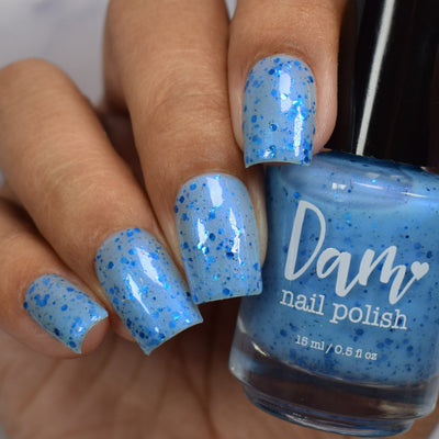 Blueberry Sanctuary by Dam Nail Polish, sheer powder blue holographic shimmer flakie crelly with metallic blue dot and shard glitters, on a light-medium skin tone hand