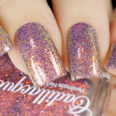Multichrome flake and holographic glitter Cadillacquer nail polish in You Wished For This, swatched on five short square nails showing a dense scatter of iridescent micro flakes shifting from rosy mauve through gold-amber, red-orange, and violet with scattered silver and blue holographic glitter particles, on light skin tone, under direct flash lighting, swatched by @yyulia_m