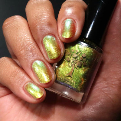 Flame On by Danglefoot Nail Polish, gold-green duochrome shimmer bottle held in a medium hand