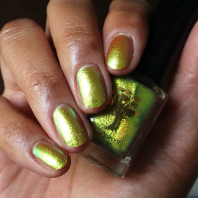 Flame On by Danglefoot Nail Polish, gold-green duochrome shimmer bottle held in a medium-deep hand