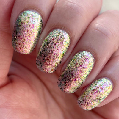Ayla the Scoliosis Dolphin by Dam Nail Polish, multichrome flakie showing mixed-size pink, gold, and green-gold shifting flakies in bright daylight, on a light skin tone hand