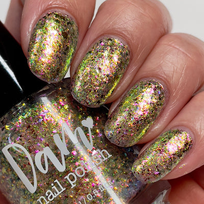 Ayla the Scoliosis Dolphin by Dam Nail Polish, blue-gold multichrome flakie with gold, pink, and blue-to-green shifting flakies over a warm taupe base, on a light skin tone hand