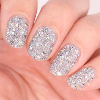 I Started the Dam Thing by Dam Nail Polish, dense silver mix of chunky hex and micro holographic glitter in studio light, on a light skin tone hand