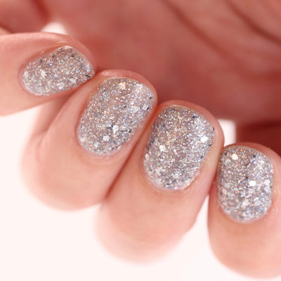 I Started the Dam Thing by Dam Nail Polish, chunky hex and micro holographic glitter with iridescent white-silver highlights in studio light, on a light skin tone hand