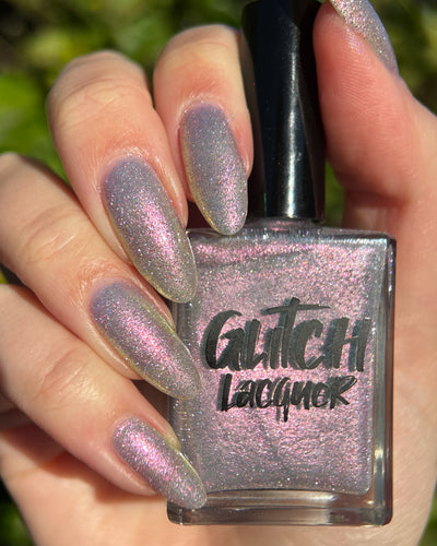 Lavender Haze by Glitch Lacquer, very light purple polish with pink-yellow-green-teal multichrome reflect and sparkly red reflective glitters, swatched on five almond nails alongside the bottle, light skin tone, bright daylight.