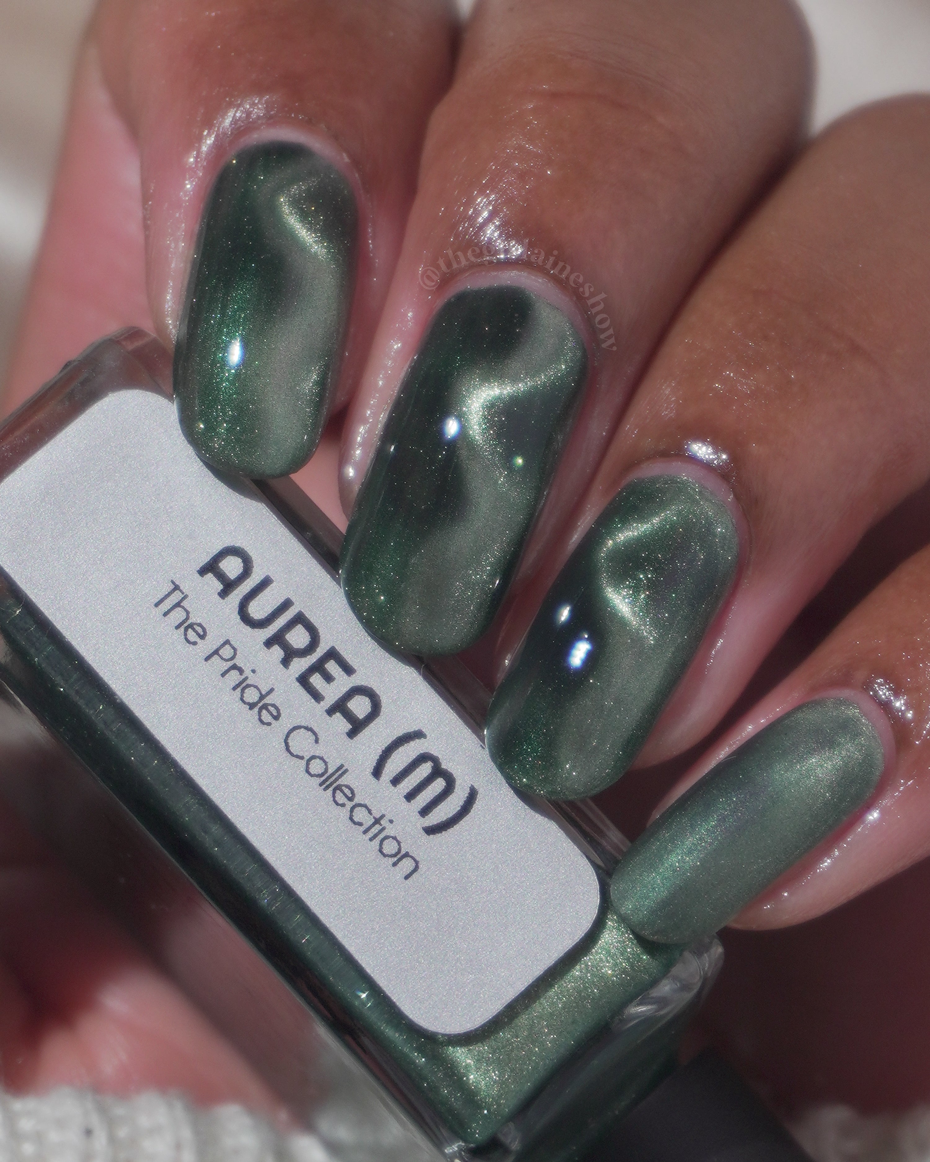 AUREA by Glitch Lacquer, blackened green base with greenish-gold magnetic cat-eye, bottle in hand on light-medium skin