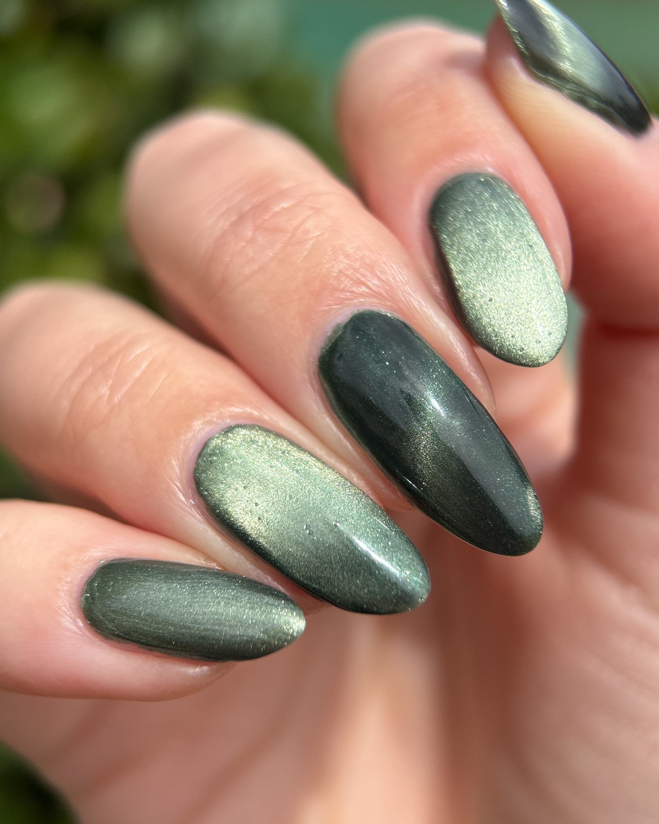 AUREA by Glitch Lacquer, blackened green base, greenish-gold magnetic cat-eye, on light skin tone almond nails