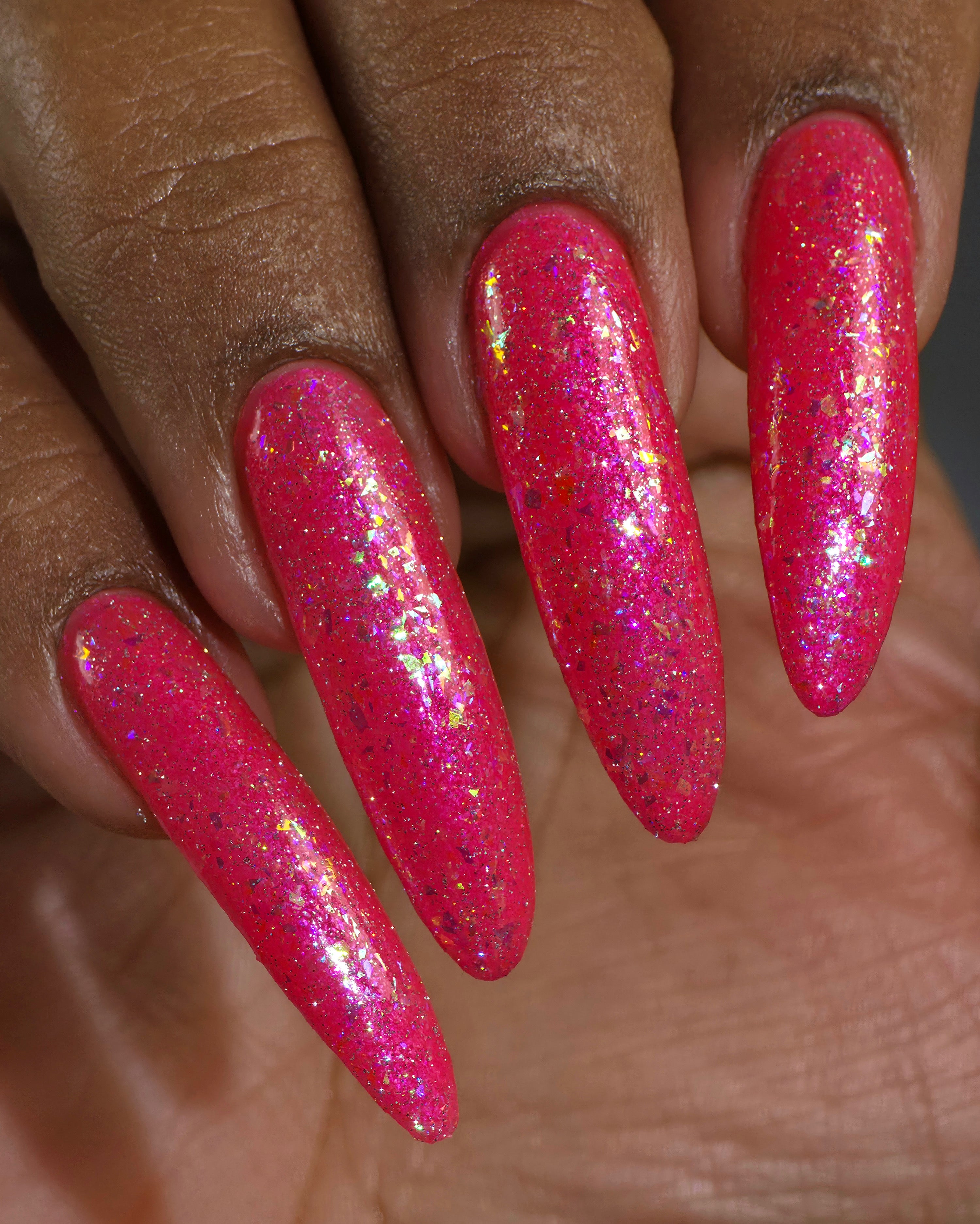 Be Gay, Do Crime by Glitch Lacquer, silver holo glitter and rainbow flake topper over coral red, on deep skin tone nails