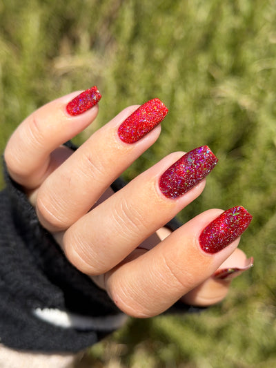 Be Gay, Do Crime by Glitch Lacquer, silver holo glitter and rainbow flake topper over red, on light-medium skin tone square nails