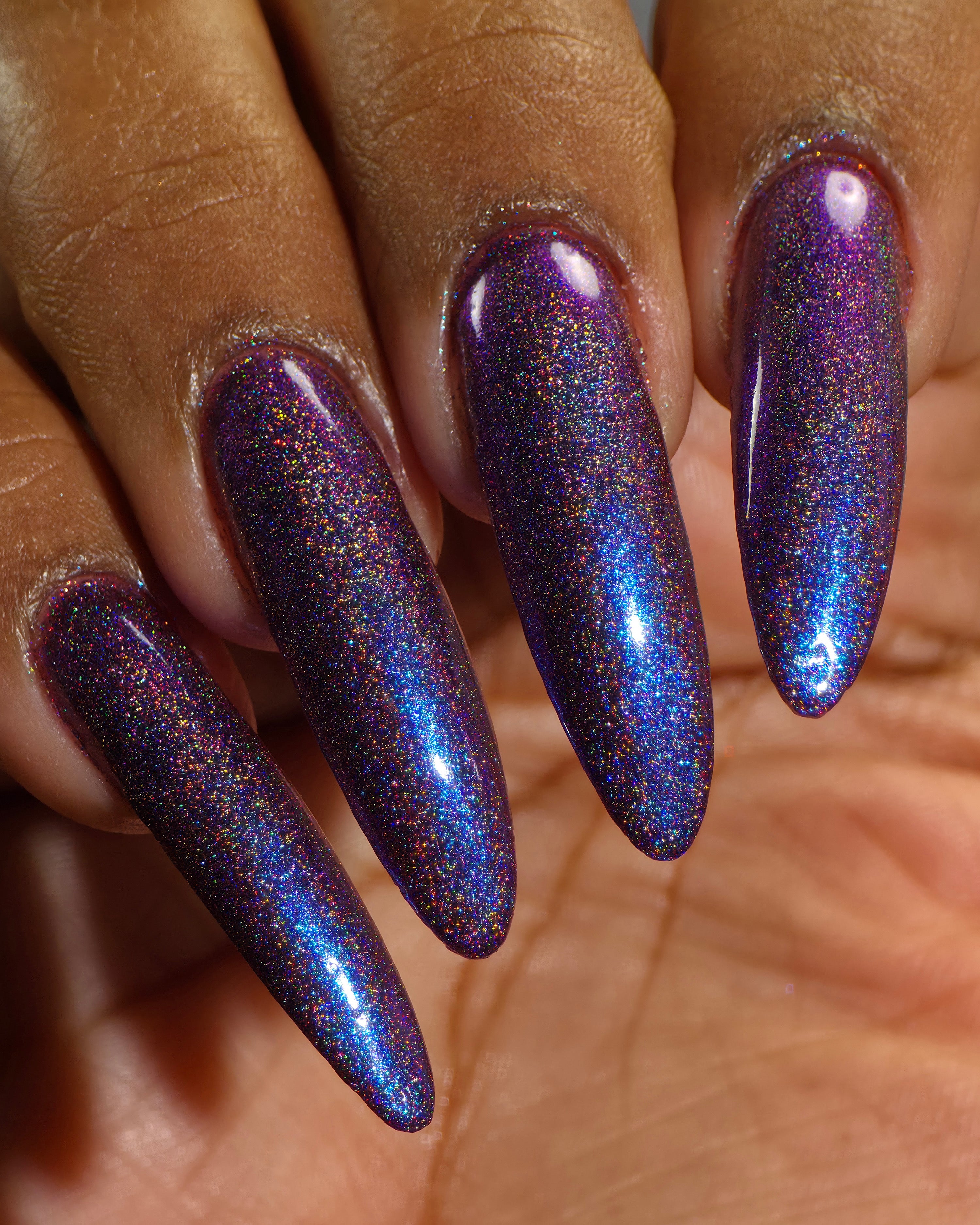 Bi Panic by Glitch Lacquer, magenta jelly, blue-to-purple glow, linear holographic, on deep skin tone stiletto nails