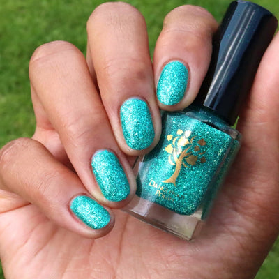 Mutant and Proud by Danglefoot Nail Polish, green-teal holographic reflective glitter flakie bottle held in a medium hand