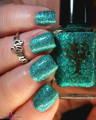 Mutant and Proud by Danglefoot Nail Polish, green-teal holographic reflective glitter flakie bottle held in a light hand