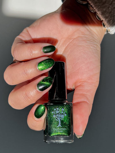 New Divide by Danglefoot Nail Polish, green shimmer jelly magnetic bottle held in a light hand