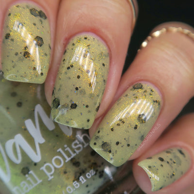 OG Devo-tea by Dam Nail Polish, pale sage-tan crelly with dense gold shimmer and scattered black hexagonal and dot glitters, on a light skin tone hand
