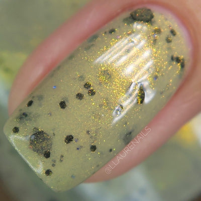 OG Devo-tea by Dam Nail Polish, macro close-up of muted olive-tan crelly base with dense gold shimmer and assorted black glitters from micro dots to chunky hex