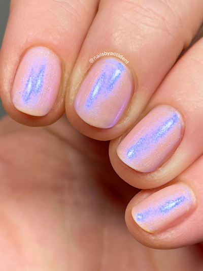 A Whimsical Dream by Dam Nail Polish, sheer blush pink base with streaky blue-purple duochrome shimmer intensified in bright daylight, on a light skin tone hand