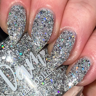 I Started the Dam Thing by Dam Nail Polish, silver reflective and holographic glitter bomb under direct flash, blinding with iridescent rainbow sparks, on a light skin tone hand