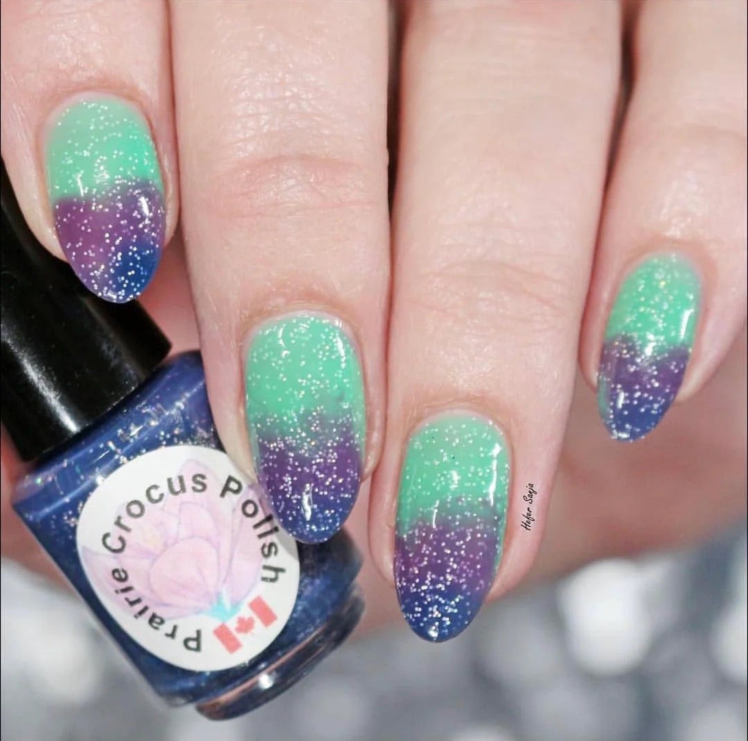 Prairie Crocus Polish Mermaid Tail thermal polish on long nails showing all three temperature states simultaneously: blue at tips, purple through middle, green at base, loaded with holographic glitter, light skin tone — @hefersanja