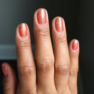 Protector of the Deep by Danglefoot Nail Polish, orange-pink reflective shimmer glitter on a medium skin tone hand