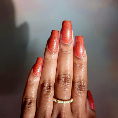 Protector of the Deep by Danglefoot Nail Polish, orange-pink reflective shimmer glitter on a medium-deep skin tone hand