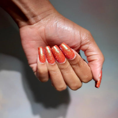 Protector of the Deep by Danglefoot Nail Polish, orange-pink reflective shimmer glitter on a medium-deep skin tone hand